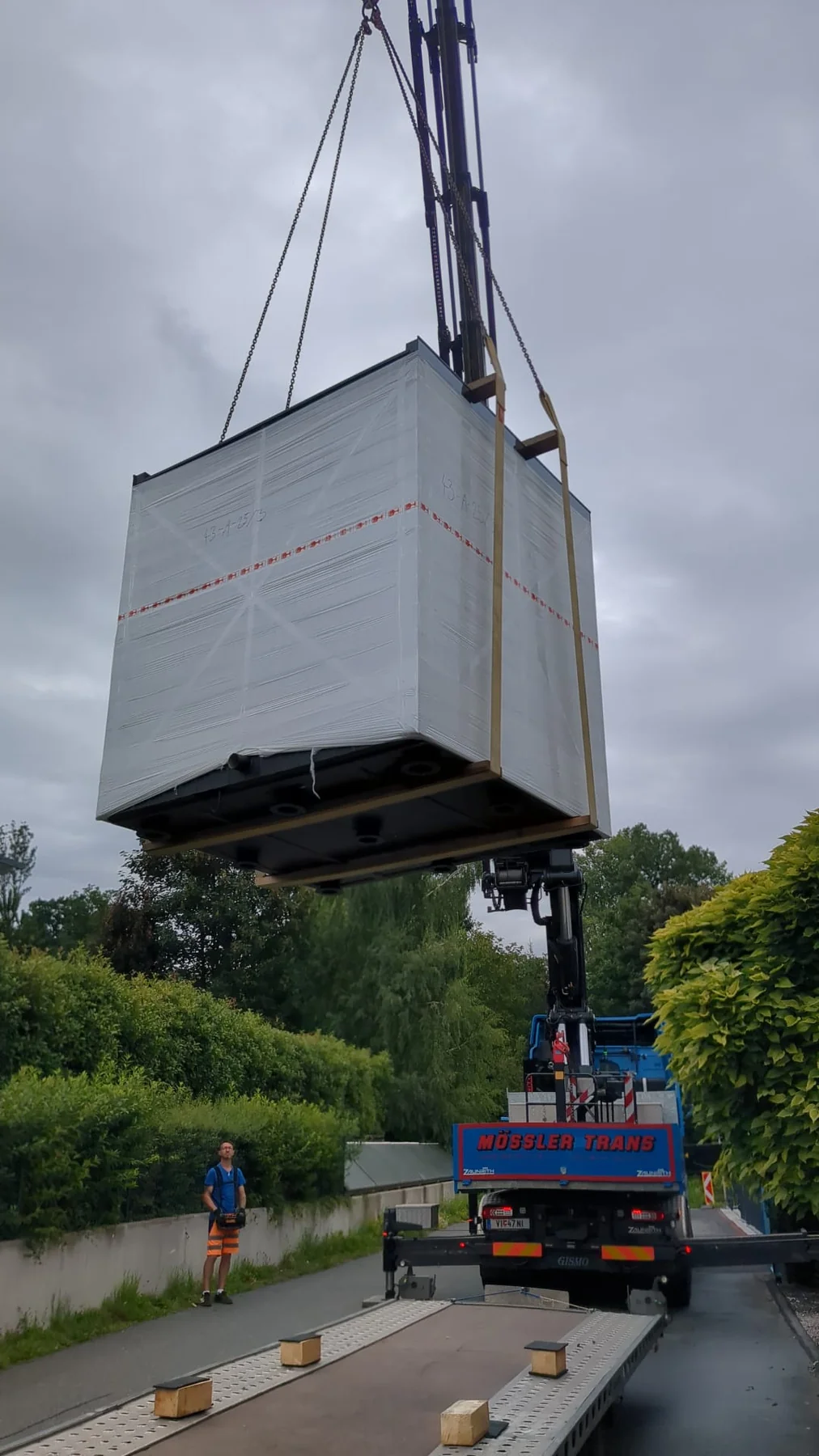 A crane lifting a complete wrapped prefabricated unit from a trailer