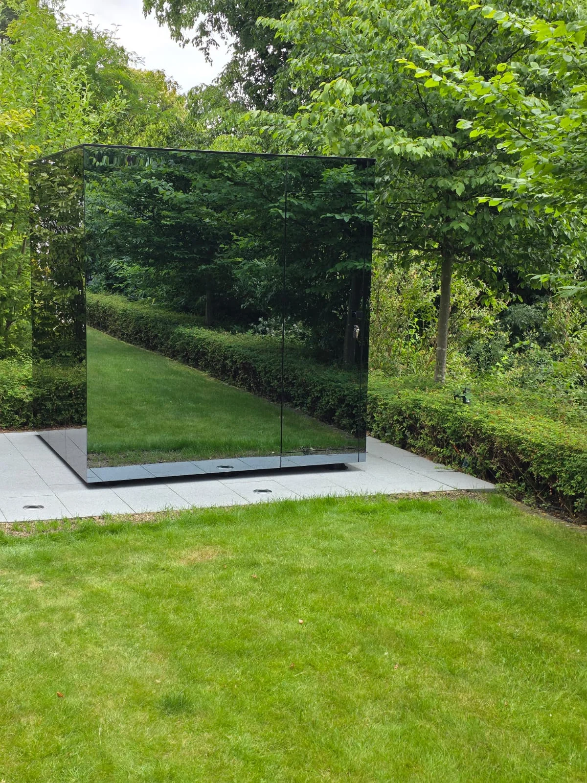 Mirror+ exterior reflecting lawn and mature trees, blending into a lush garden